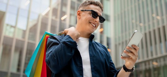 Un home mirando o seu teléfono con bolsas de roupa